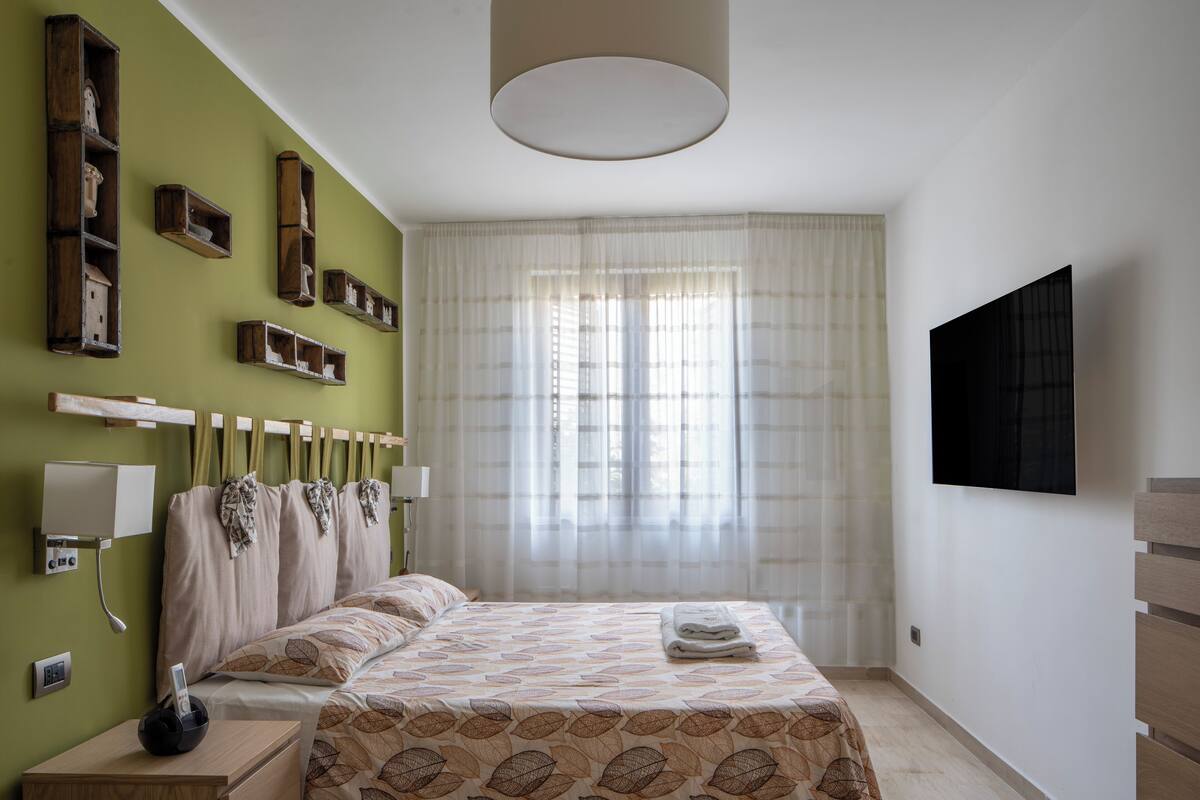 A bedroom with a bed, bedside table, lamp, and a TV mounted on the wall.