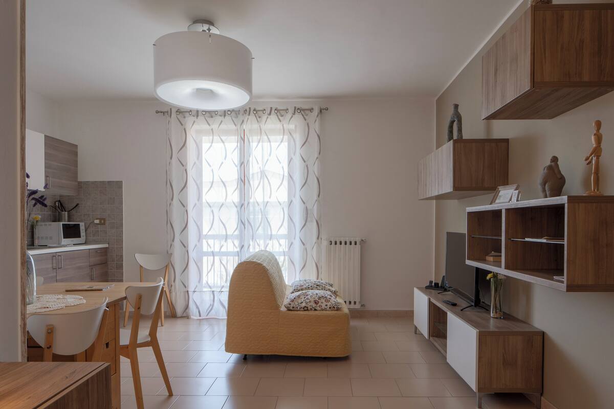 A modern living room with a sofa, a dining table with chairs, a TV, and built-in wooden shelves.