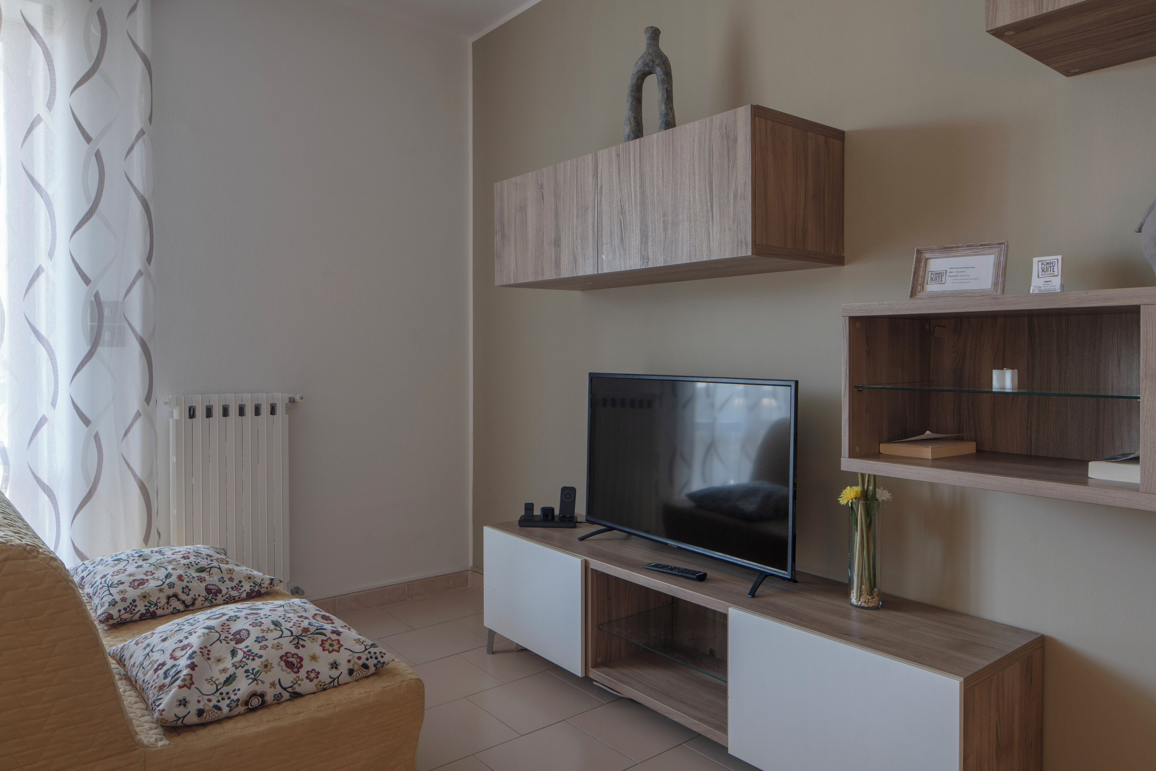 Una sala moderna con televisor de pantalla plana, estanterías de madera, un radiador y un sofá estampado.