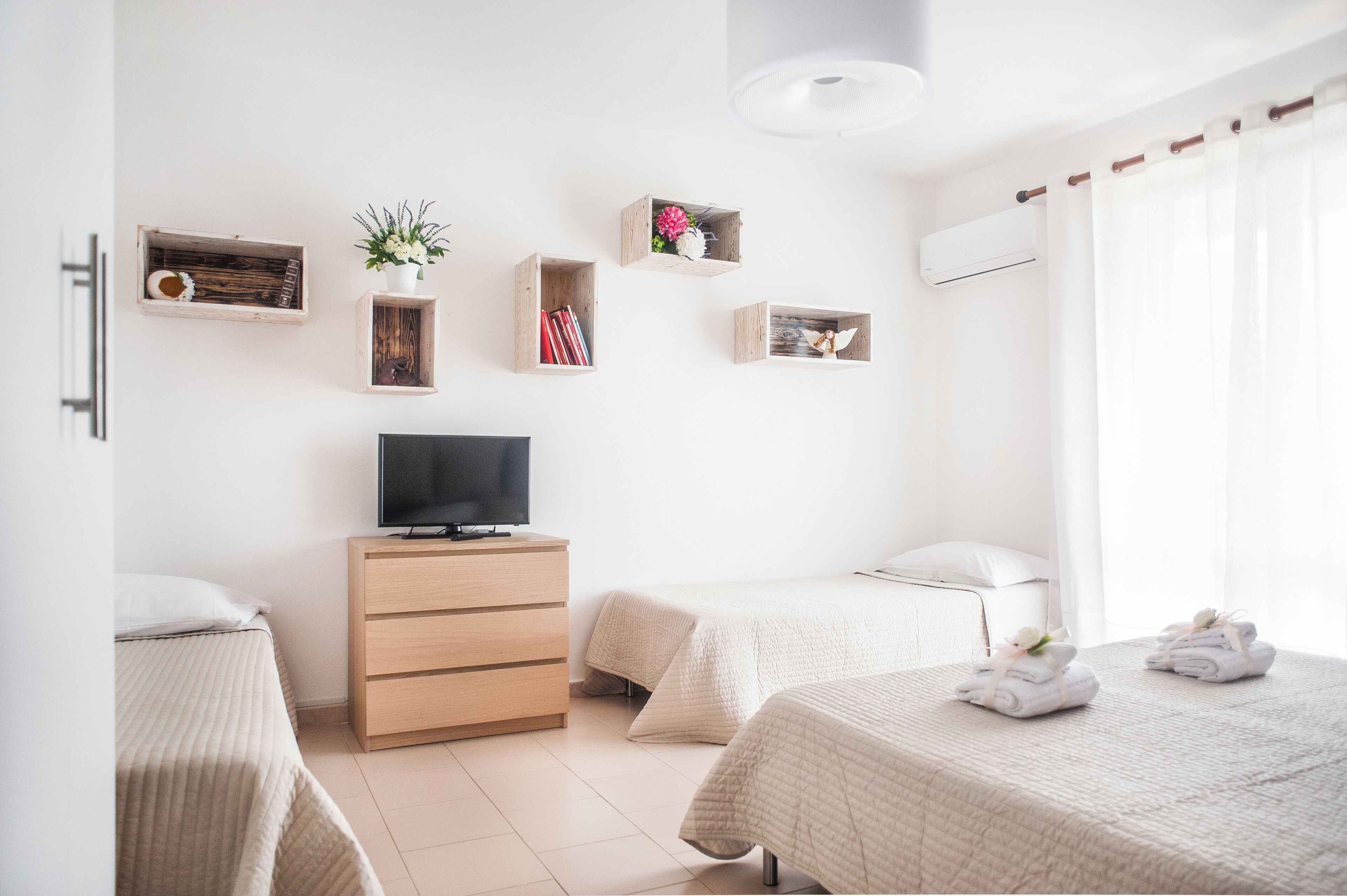 Een moderne hotelkamer met twee bedden, een televisie, houten opbergmeubels en een raam met gordijnen.