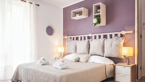 Ein ordentlich bezogenes Bett mit einer gesteppten Decke, zwei Nachttische mit Lampen und ein an der Wand befestigtes Regal mit Dekoration.