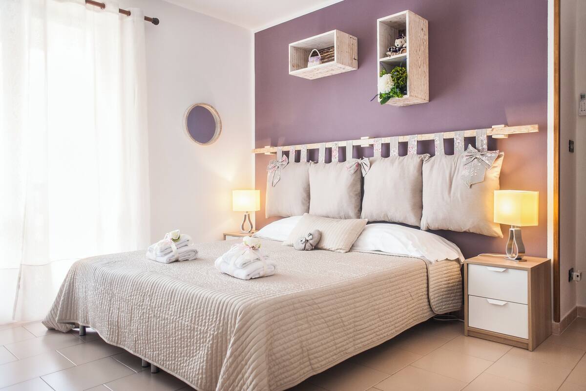 A neatly made bed with a quilted cover, two bedside tables with lamps, and a wall-mounted shelf with decorative items.