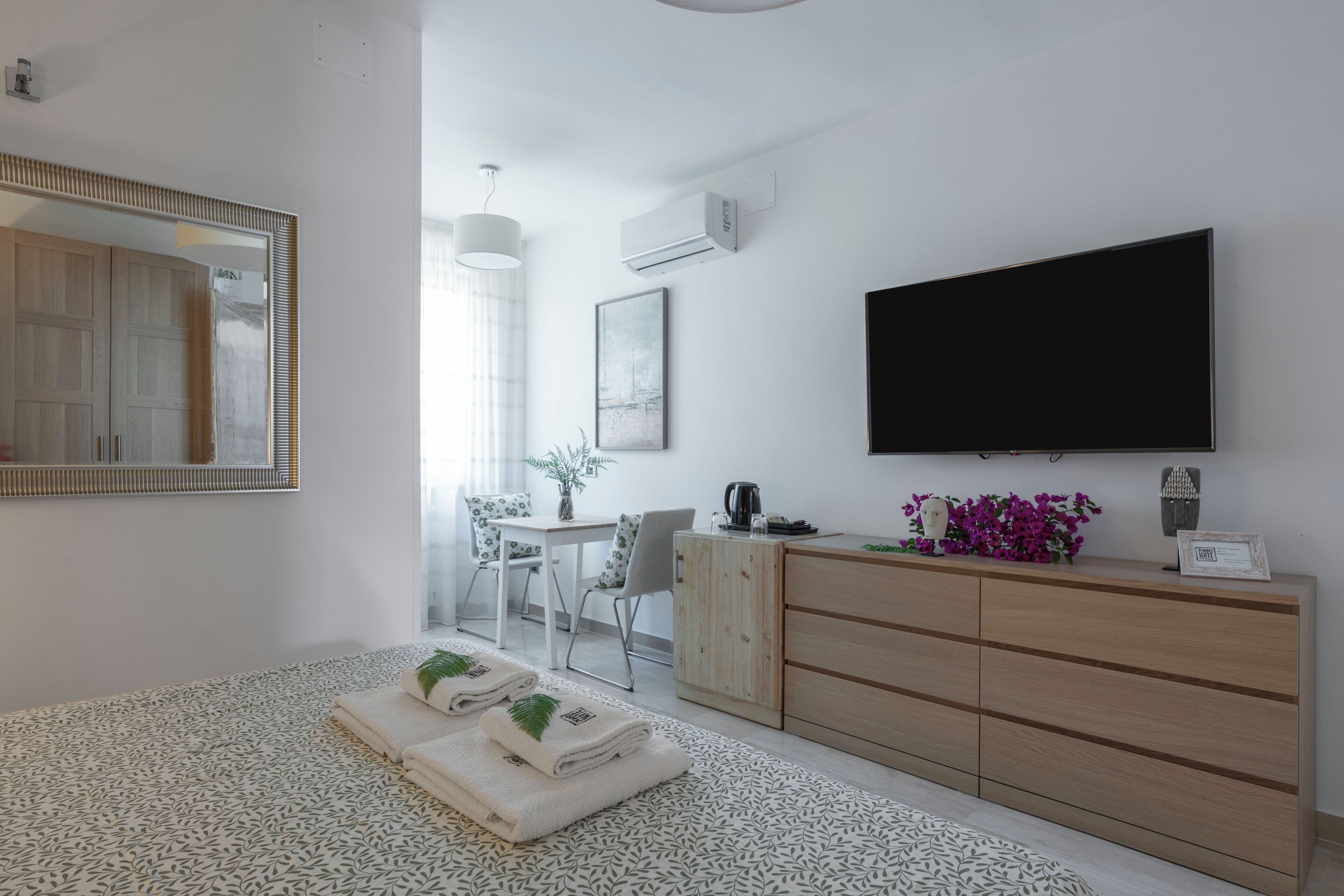 Ein modernes Schlafzimmer mit einem Bett, einer Holzkommode, einem Fernseher und einem Schreibtisch mit Stühlen.