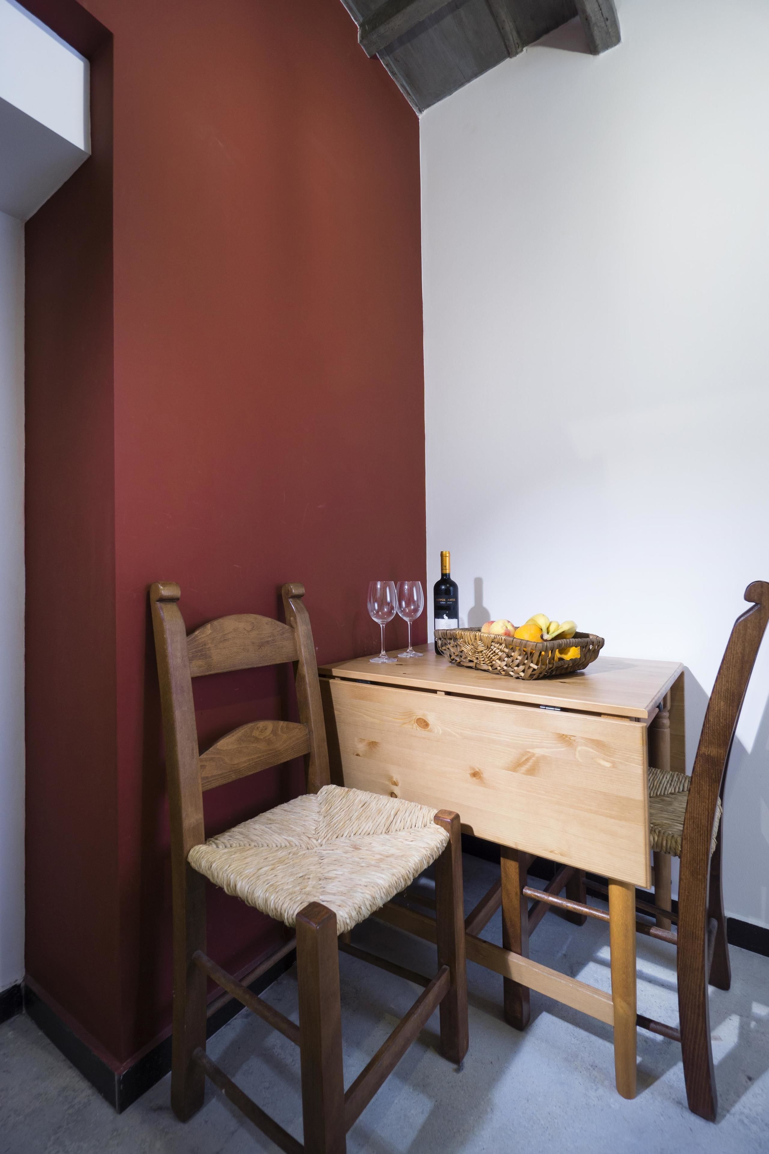 Een eethoek met een houten tafel, twee stoelen, een mand met fruit en een fles wijn.