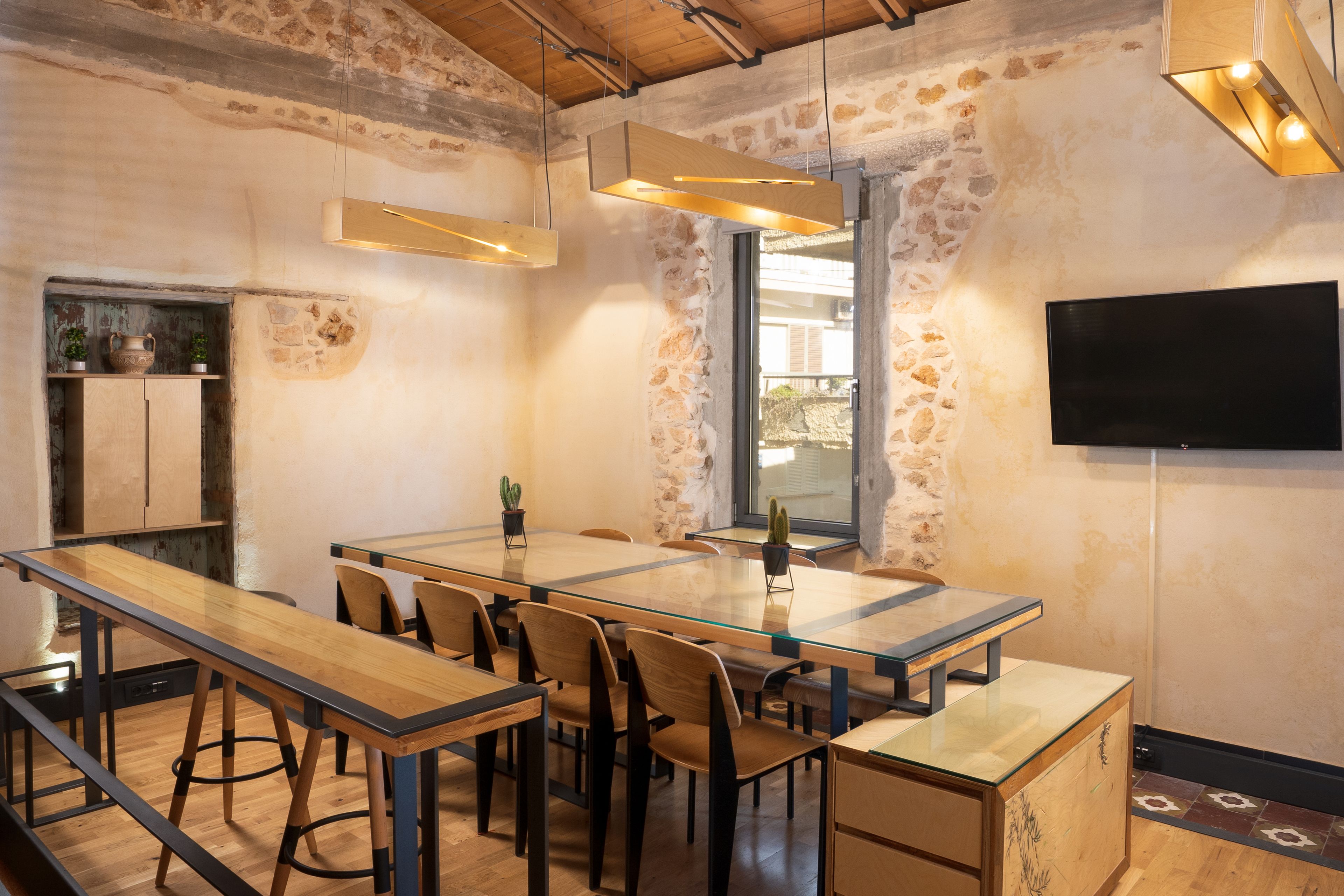 A conference room with a long table, chairs, a TV, and a stone wall.