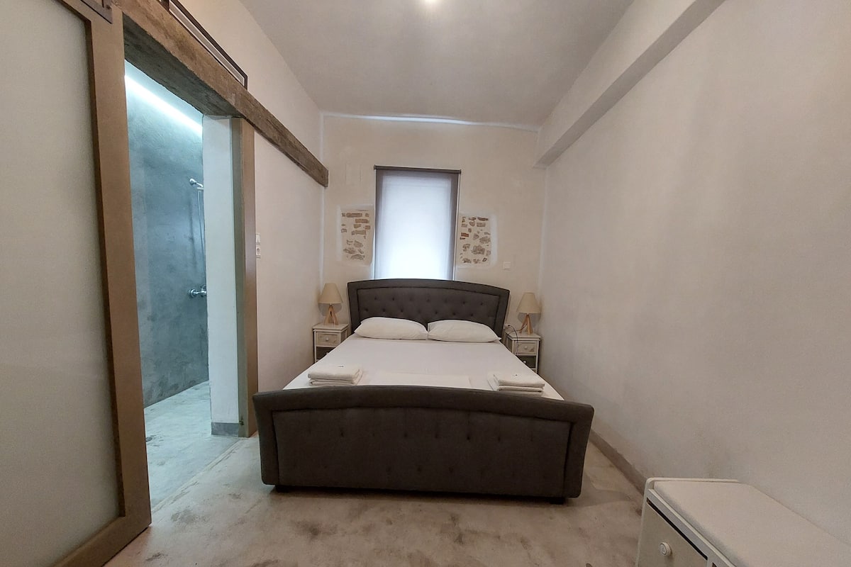 Ein Schlafzimmer mit einem großen Bett, zwei Nachttischen, einer kleinen Nachttischlampe und einer Tür zu einem weiteren Raum.