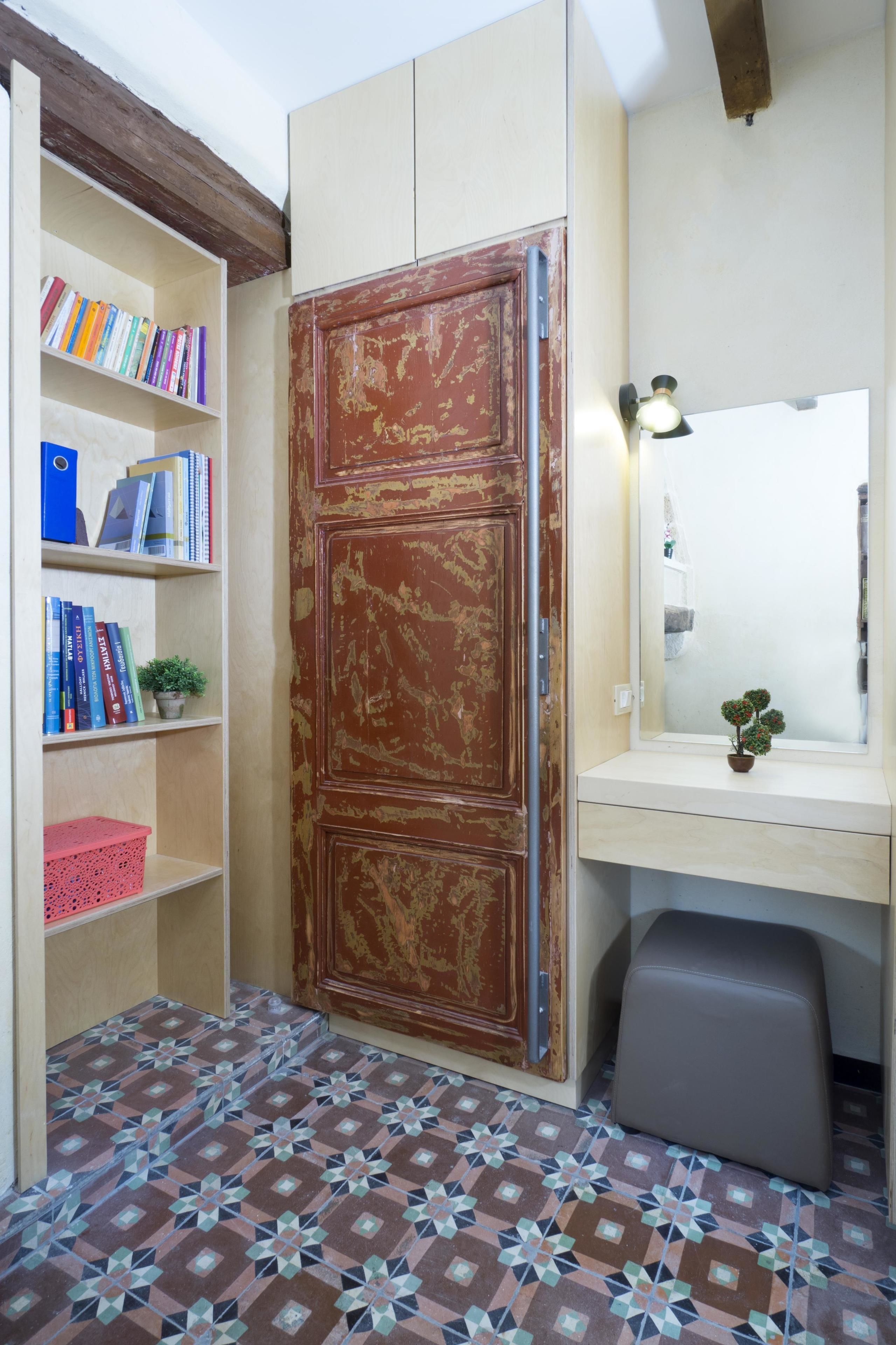 Een kamer met een boekenkast, een bureau met spiegel, een kleine plant en een vloer met patroon.
