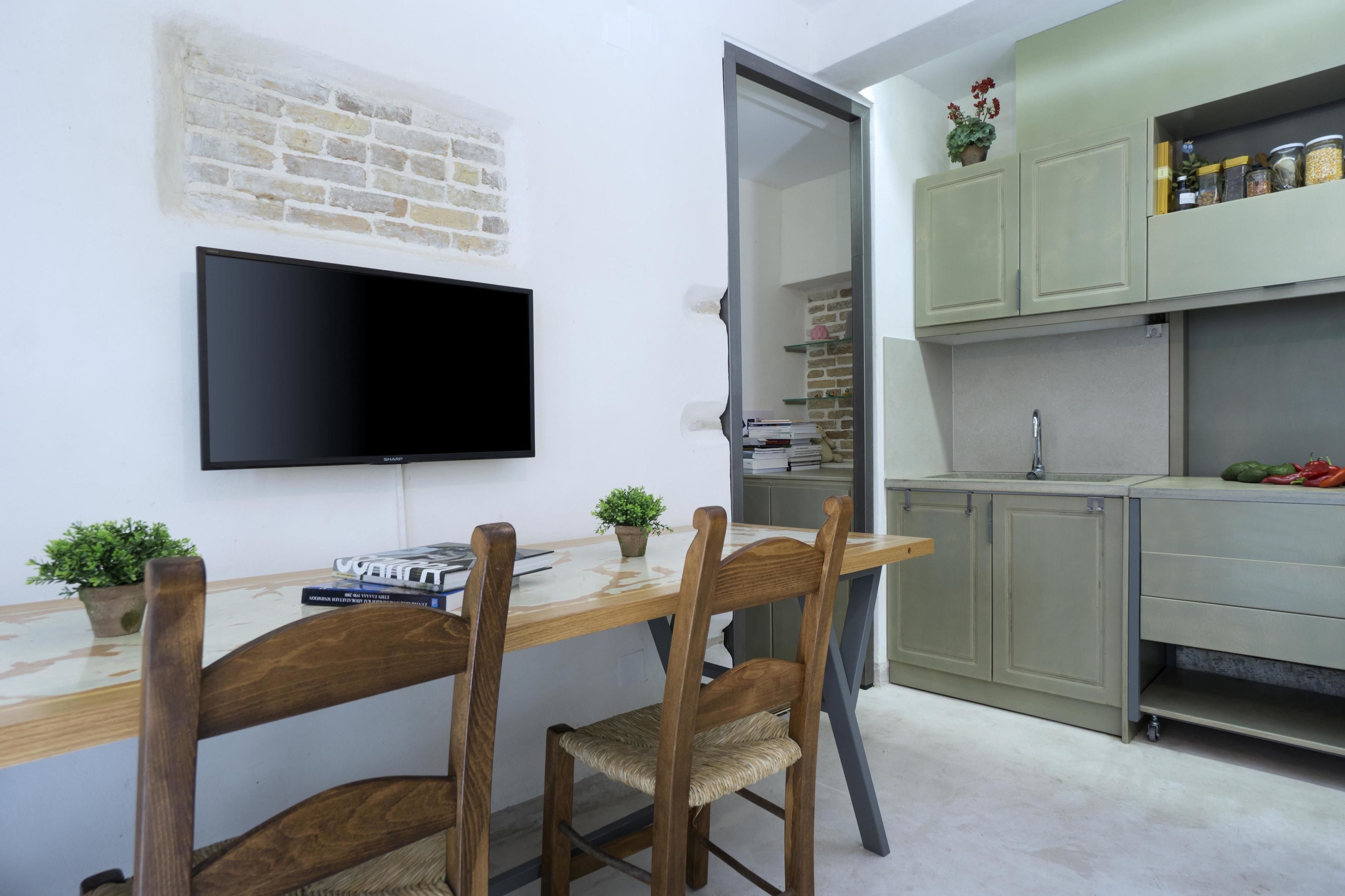 Eine kompakte Küche mit Flachbildfernseher, Holztisch und Stühlen.