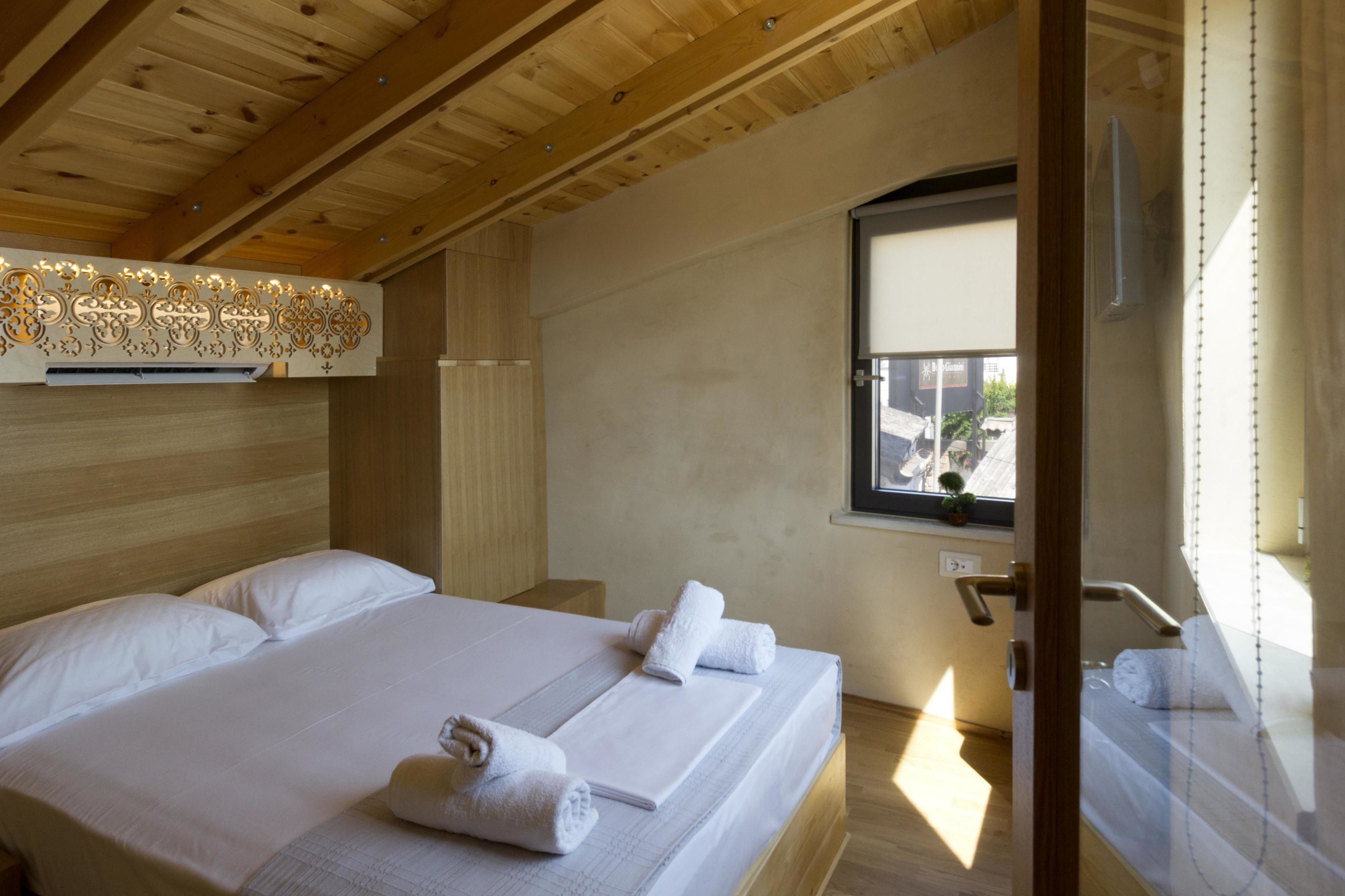 Ein Hotelzimmer mit Holzbalkendecke, einem großen Bett mit weißer Bettwäsche und einem Fenster mit Blick nach außen.