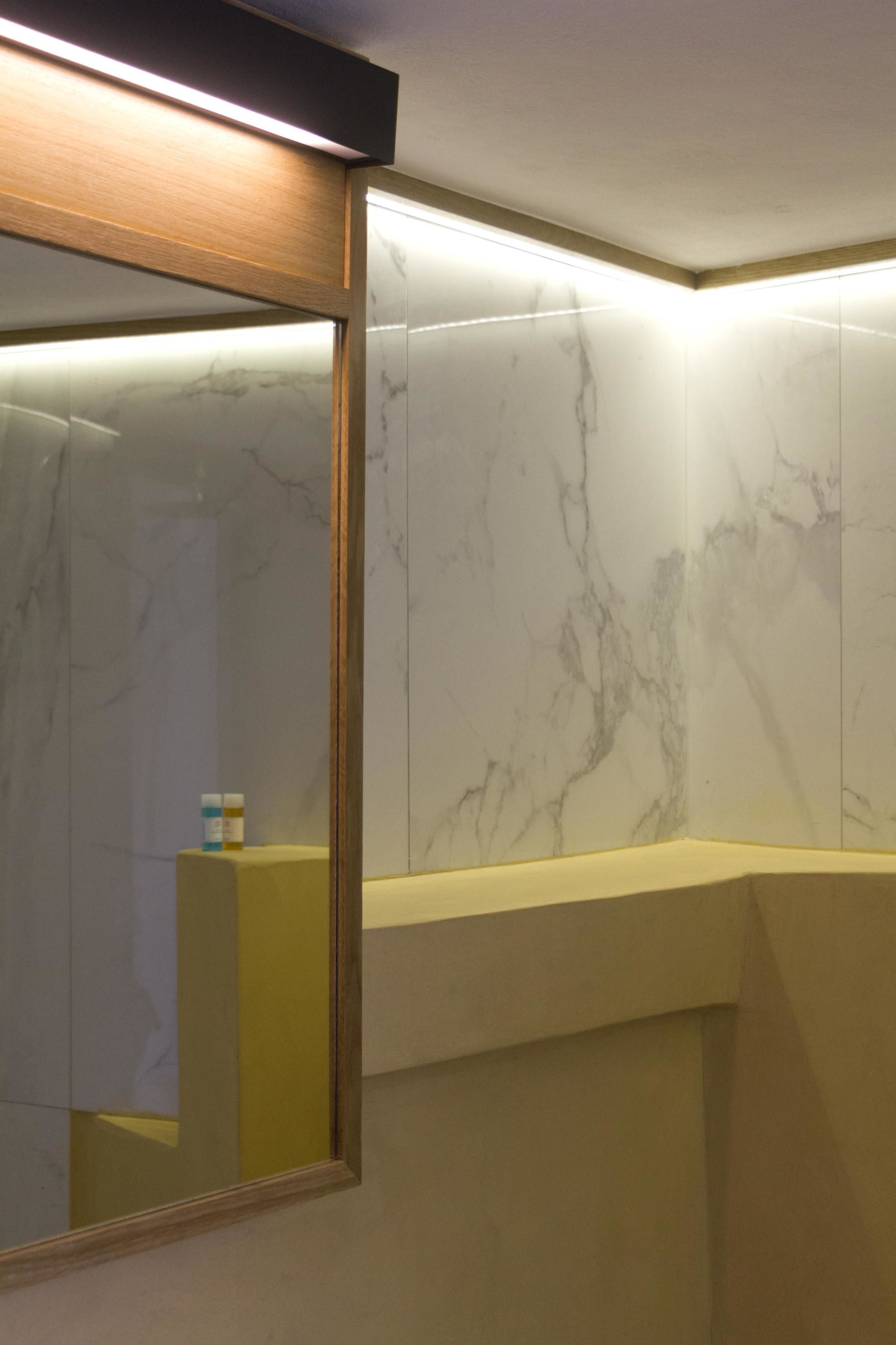 A bathroom with marble walls, a wooden-framed mirror, and a yellow countertop.