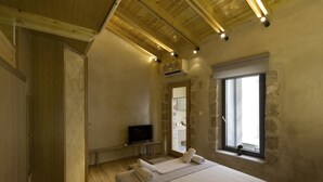 A bedroom with a wooden ceiling, a bed with white linens, a television on a small table, and a window with a view of the outside. - Evans House II (Chania)