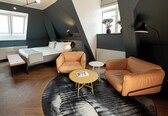 A modern bedroom with a bed, two leather sofas, a small round table, and a large window.