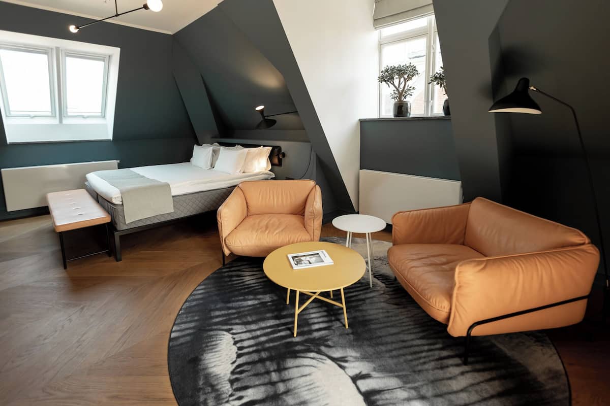 Une chambre moderne avec un lit, deux canapés en cuir, une petite table ronde et une grande fenêtre.