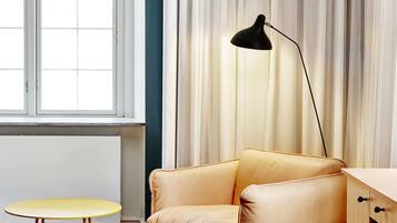 Una habitación con sofá de cuero, una mesita redonda pequeña, una lámpara de pie y vistas a través de una ventana con cortinas.