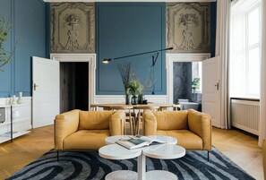 A living room with a yellow sofa, a round coffee table, and a black and white striped rug.