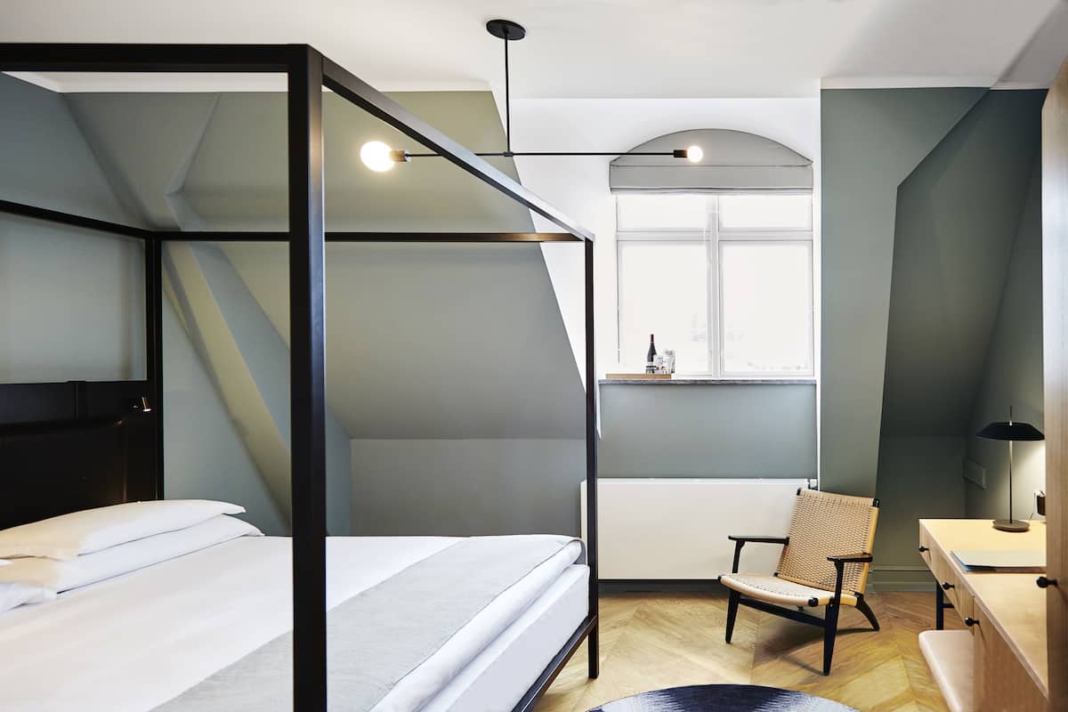 Une chambre d’hôtel moderne avec un lit à baldaquin, un bureau avec une chaise et une fenêtre donnant sur un paysage agréable.