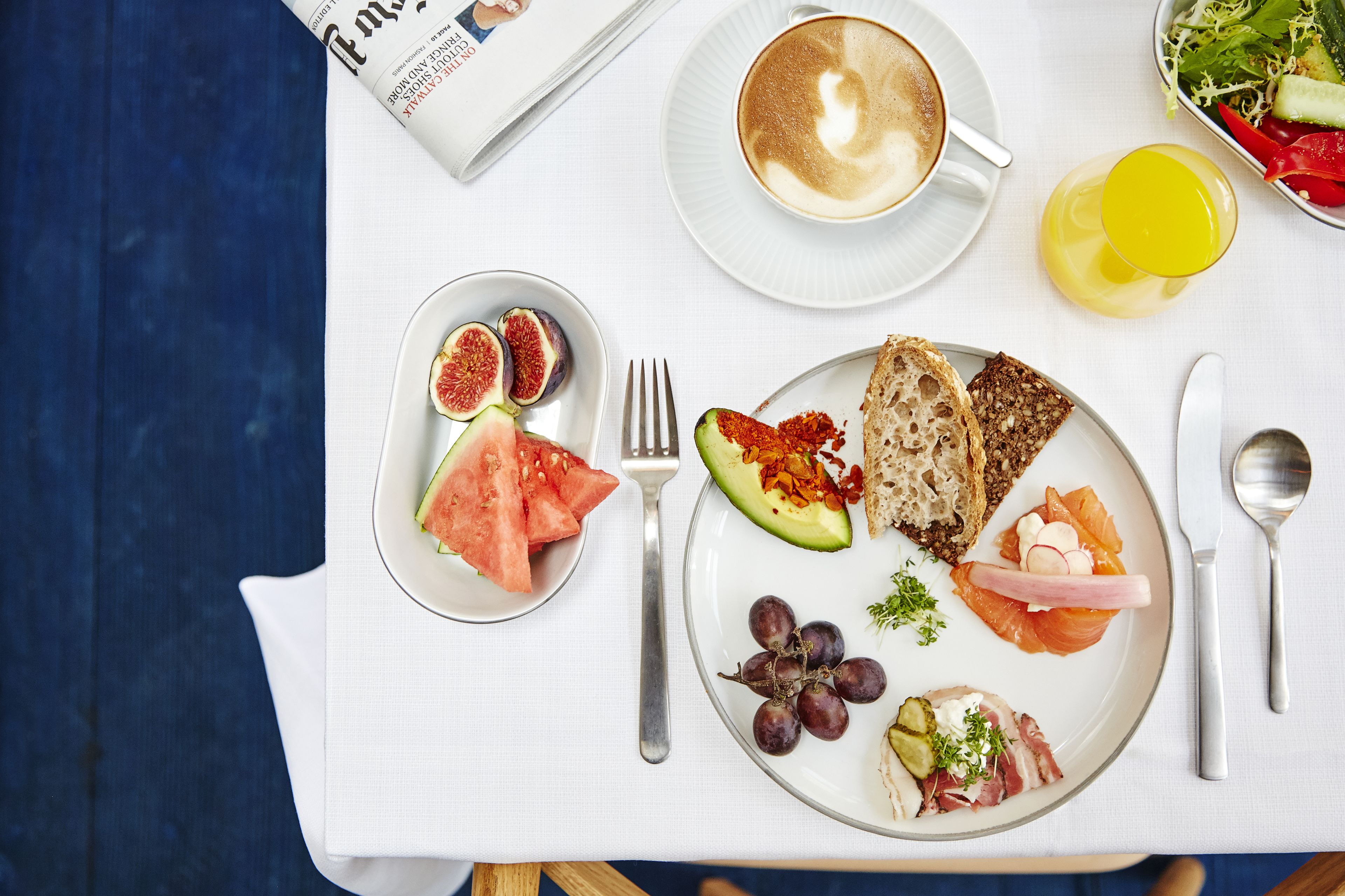 A breakfast setting with a newspaper, a cup of coffee, and various food items on a table.