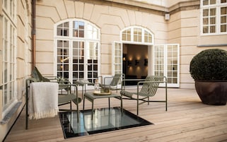 Eine Holzterrasse mit Sitzgelegenheiten im Freien, großen Fenstern und einem Blumentopf.