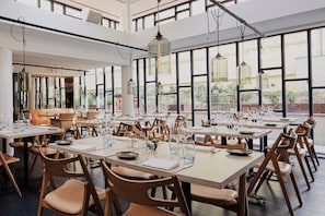 A spacious dining area with high ceilings, large windows, and modern wooden chairs. Tables are set with plates, glasses, and cutlery. - Nobis Hotel Copenhagen, a Member of Design Hotels (Copenhagen)