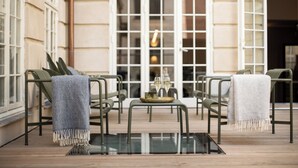 Un espace extérieur aménagé avec des chaises en métal, une table en verre et un plateau avec des verres.
