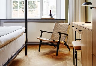 A room with a bed, a chair, a desk, and a window with curtains.