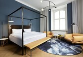 A modern bedroom with a four-poster bed, a sofa, a small round table, and a large window with curtains.