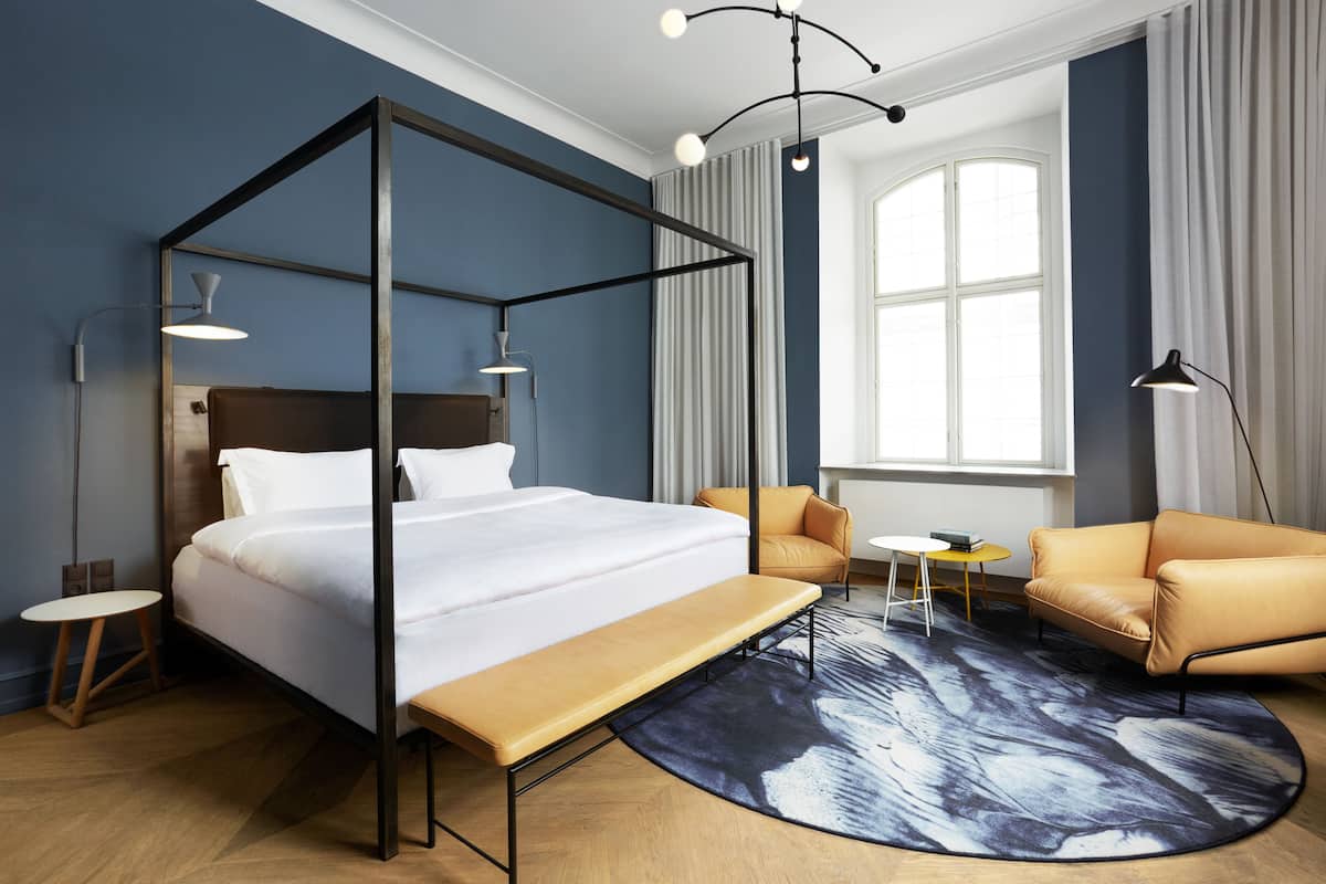 Une chambre à coucher moderne avec un lit à baldaquin, un canapé, une petite table ronde et une grande fenêtre avec des rideaux.