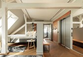 A modern loft bedroom with a sloped ceiling, a bed, a small table, and a bench.