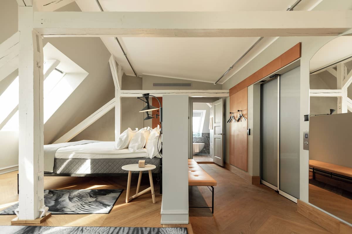 Une chambre de style loft moderne, avec un plafond en pente, un lit, une petite table et un banc.
