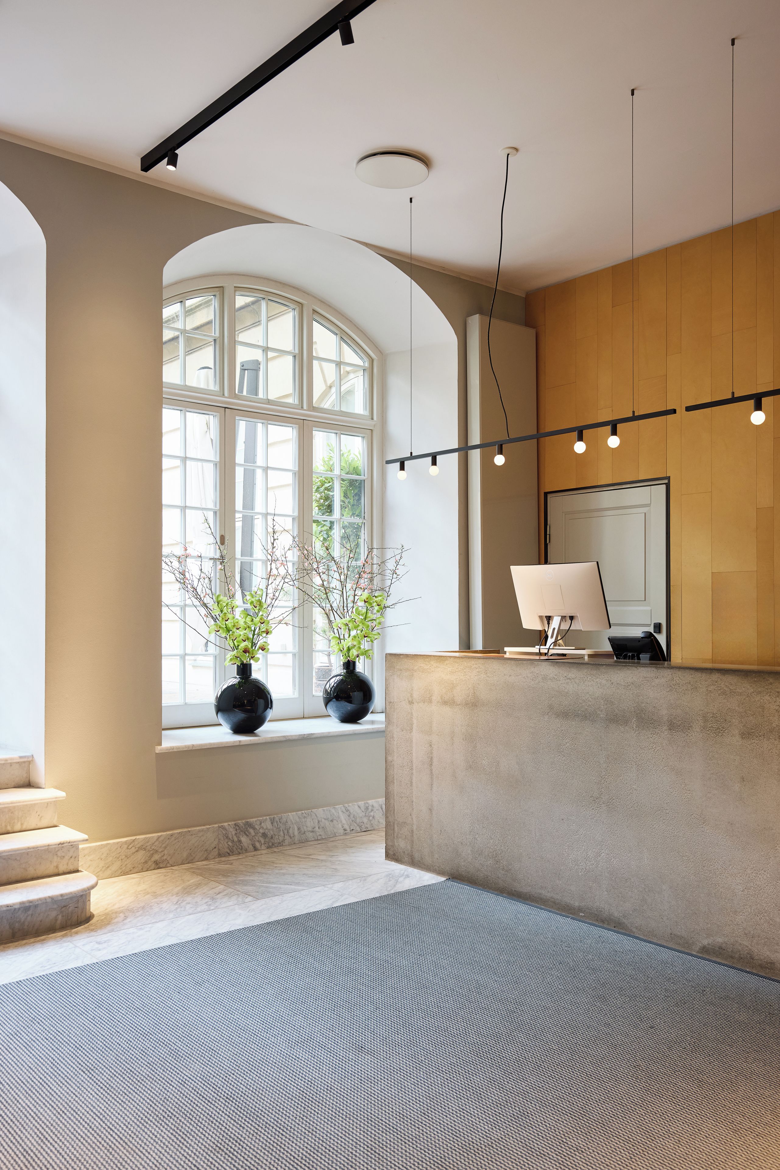 A reception area with a marble staircase, a reception desk, and a large window with plants.