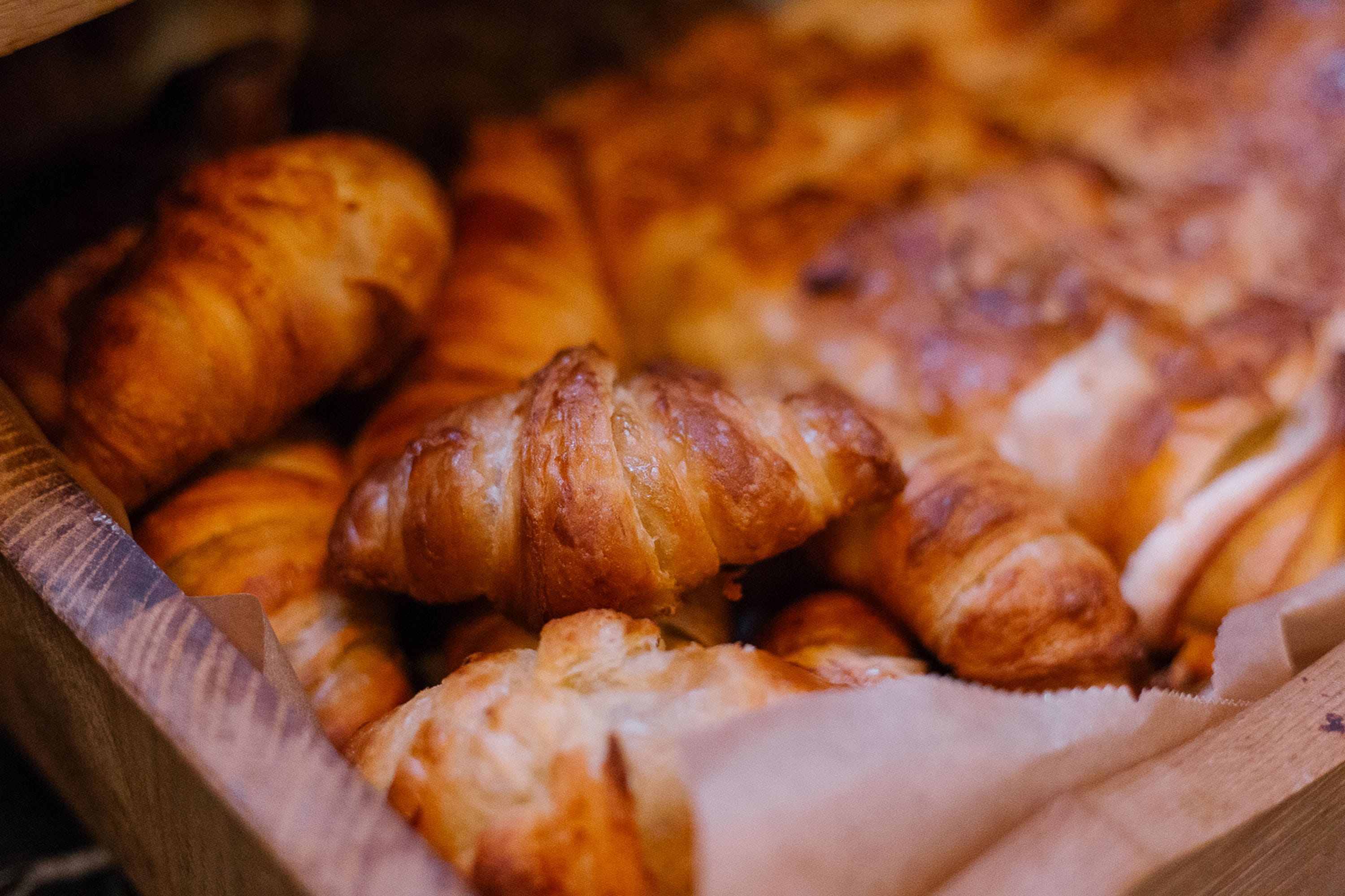 A wooden box filled with golden-brown croissants.