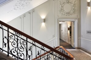 A grand staircase with ornate black railings and white walls with decorative moldings.