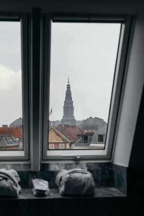 Een kamer met een raam dat uitkijkt op een stadsgezicht, inclusief een opvallende toren.