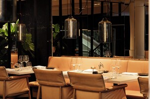 Un restaurante con una larga mesa dispuesta para comer, rodeado de asientos con cojines y lámparas colgantes.
