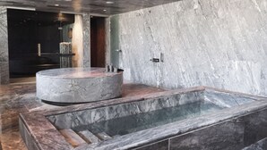 Une salle de bain moderne avec un lavabo en marbre, une baignoire intégrée et un banc en bois.