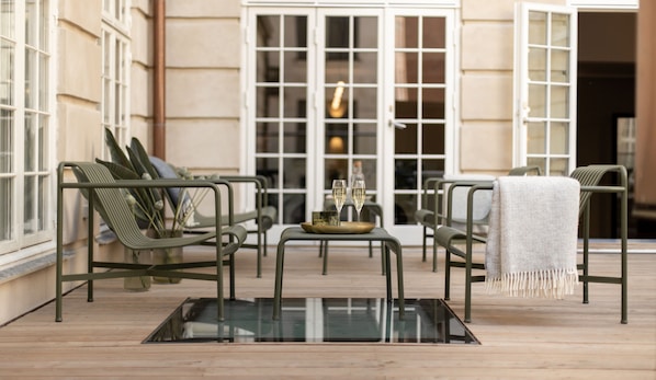 A modern outdoor seating area with metal chairs and a glass table, featuring a tray with two glasses.