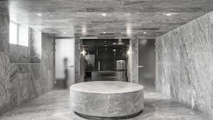 Un hall d’entrée moderne avec un élément décoratif circulaire en marbre, des murs en marbre et un ascenseur en verre.