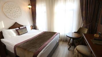 Quarto de hotel com uma cama grande, uma mesa redonda pequena, uma cadeira e uma escrivaninha com um computador e uma placa.