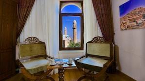 Ein Zimmer mit zwei Holzstühlen, einem kleinen Tisch mit Teekanne und Tasse, und einem Fenster mit Blick auf einen Minarett.