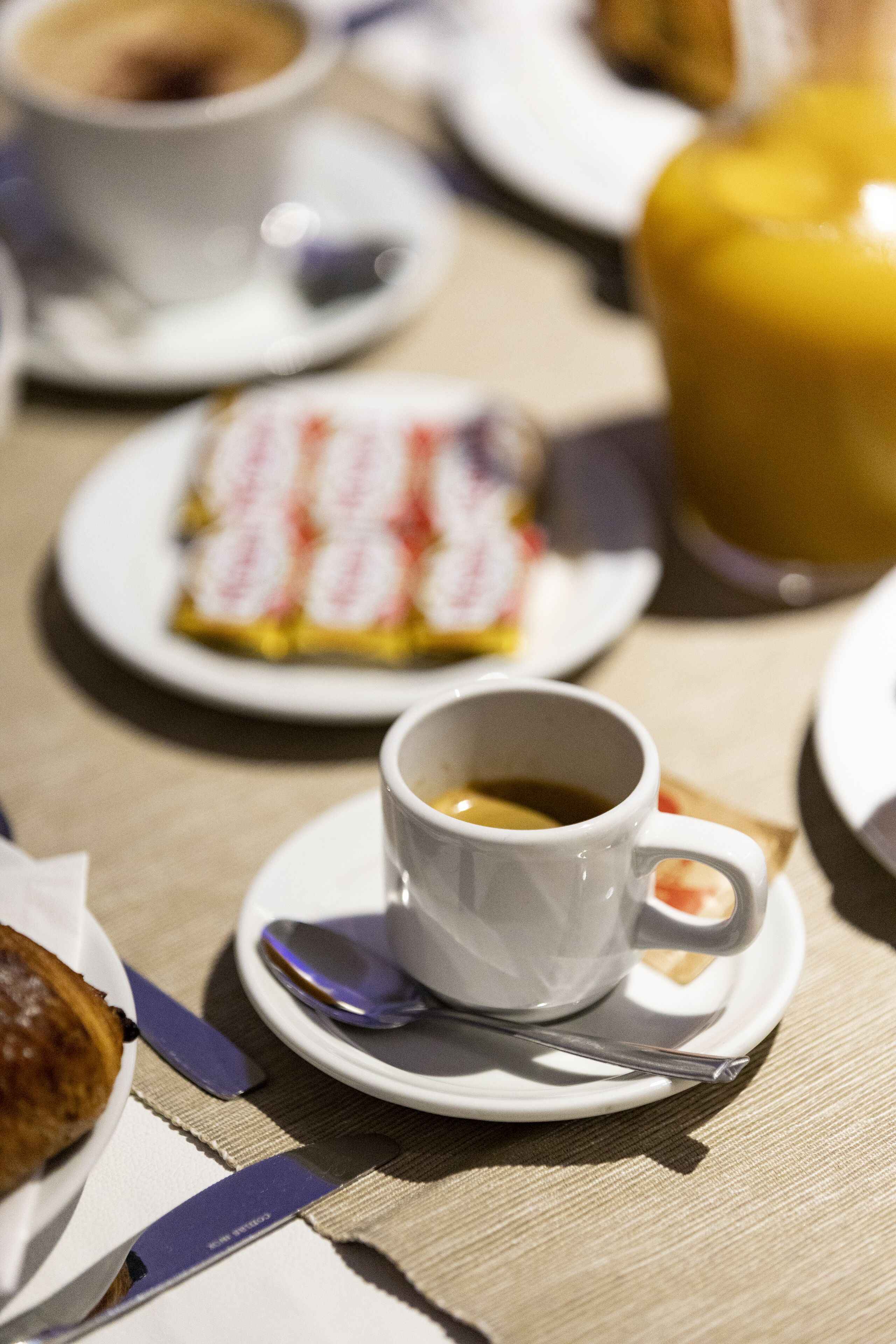 Een eettafel met een kop koffie, een bord met gebak en een gele bak.