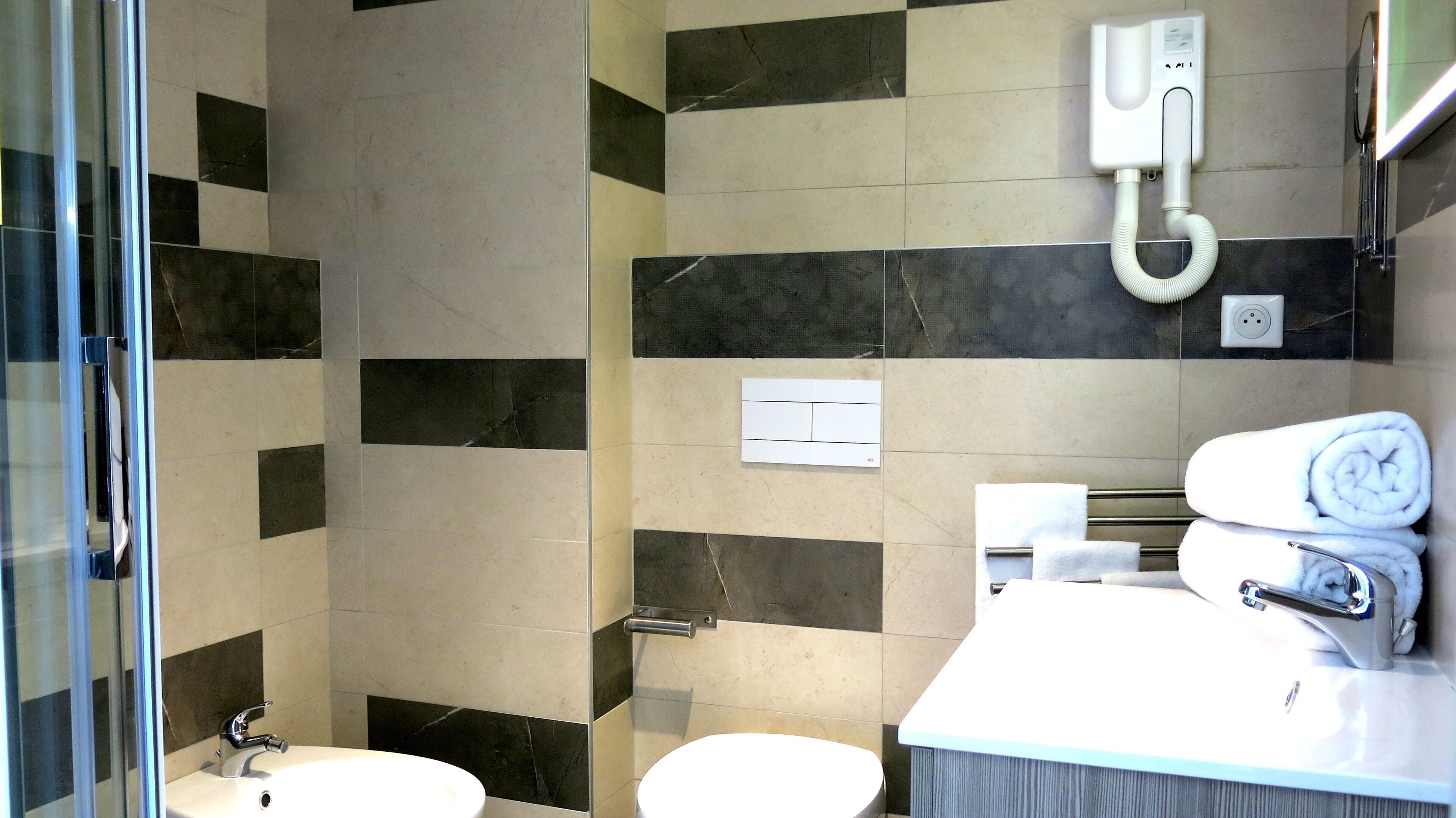Une salle de bain avec une douche à parois de verre, un lavabo, des toilettes, un porte-serviettes avec des serviettes et un sèche-cheveux fixé au mur.