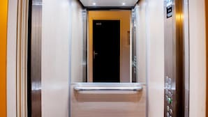 An elevator interior with a metallic finish, a door with a handle, and a control panel with buttons. - Appart'hotel Le Pelerin (Lourdes)