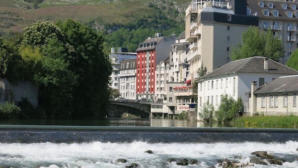 A river with a bridge, buildings with balconies, and a restaurant sign. - Appart'hotel Le Pelerin (Lourdes)