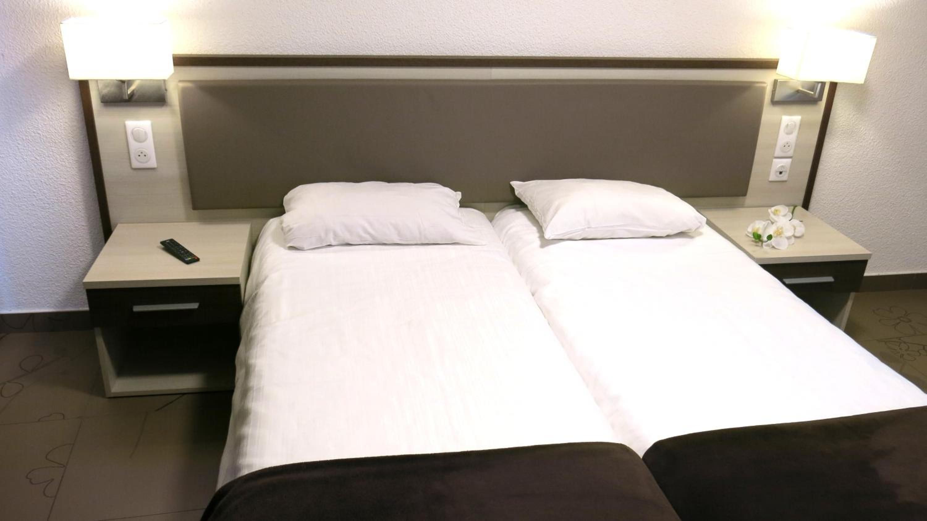 A double bed with white bedding, two bedside tables with lamps, and a remote control on the left table.