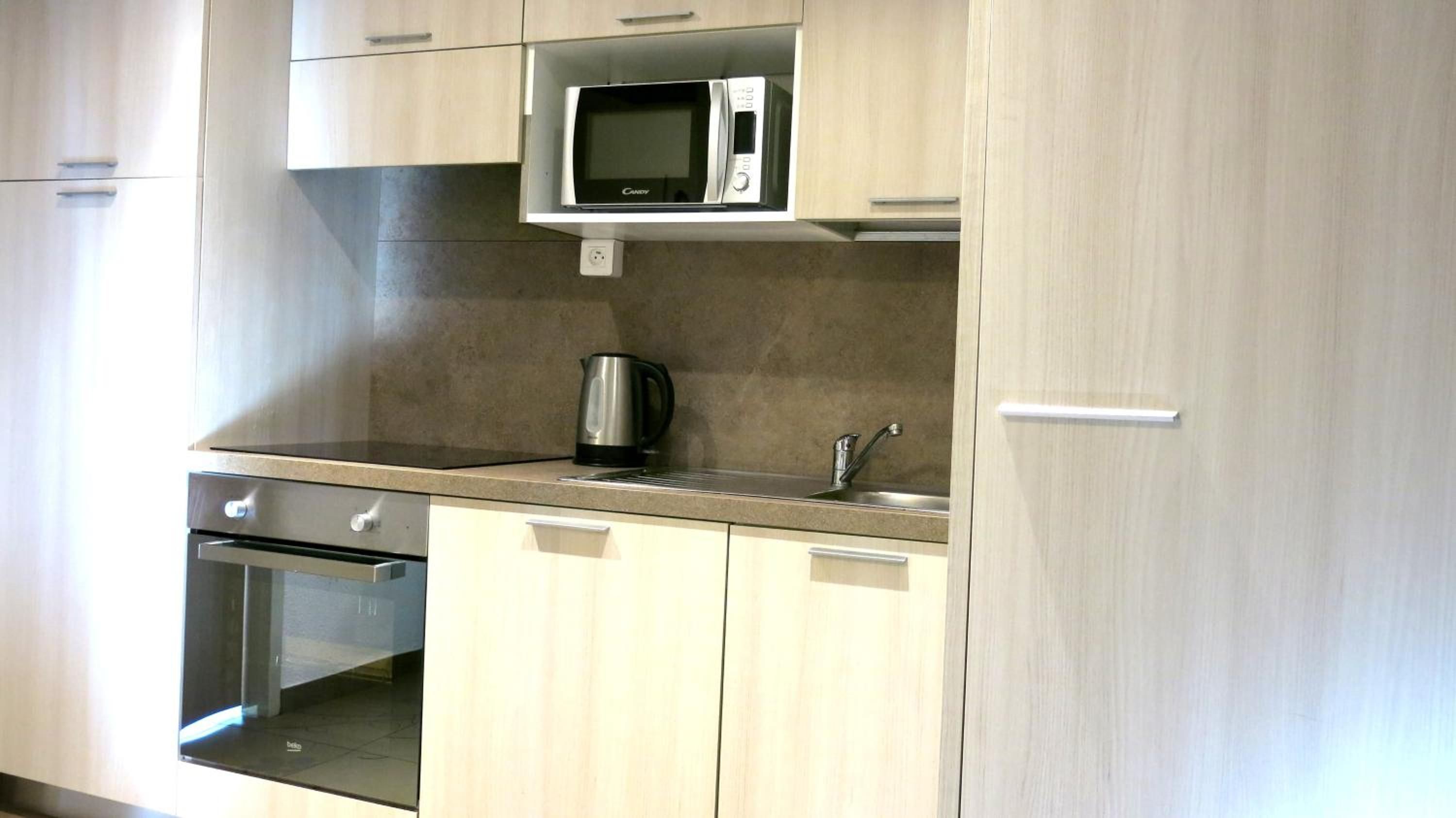 A kitchen with a built-in microwave, a kettle, and a stainless steel oven.