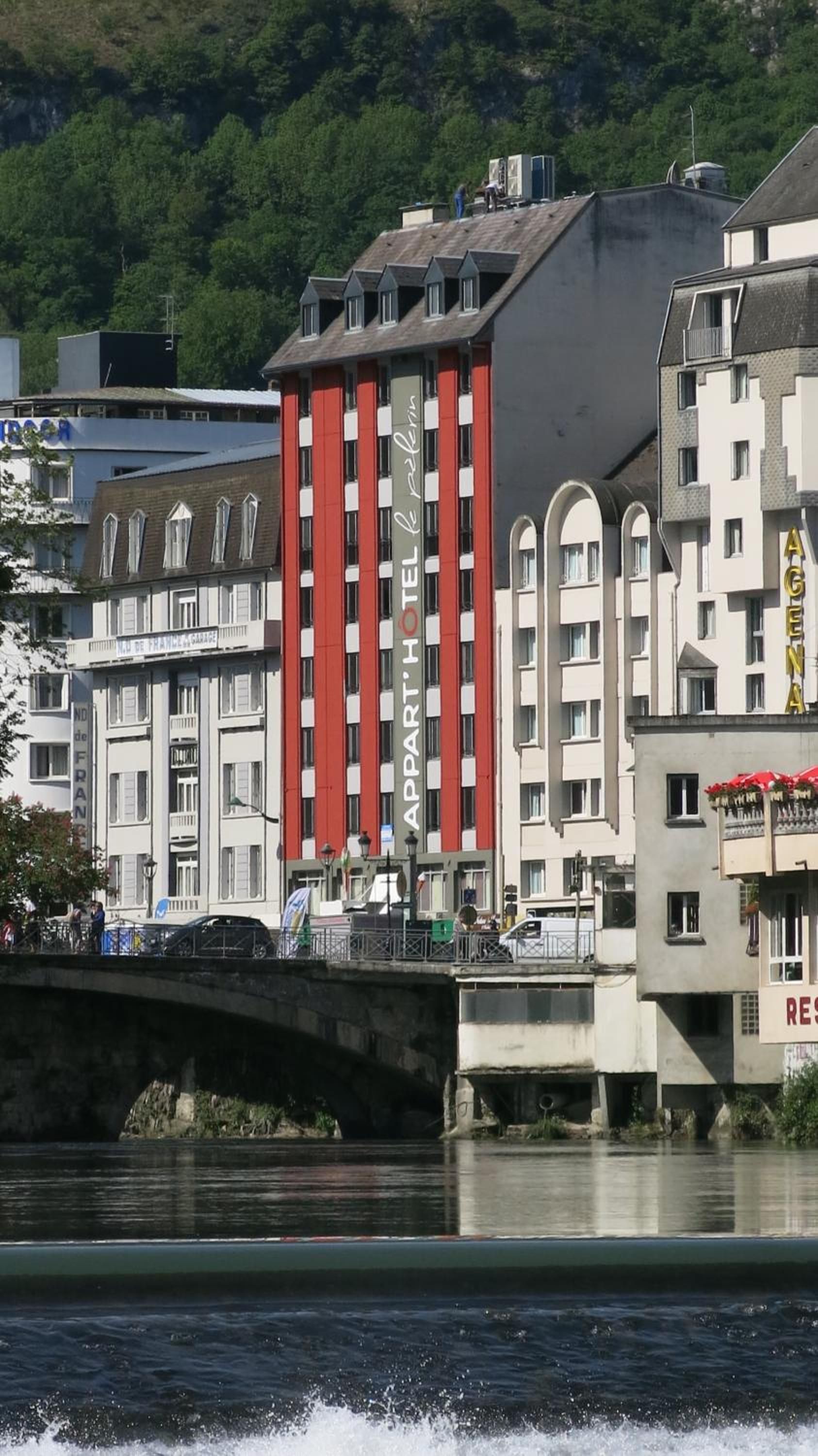 A hotel with a prominent red facade, a bridge in the foreground, and a river in the background.