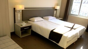 A double bed with a headboard, two bedside tables with lamps, a nightstand with a drawer, and a window with a view of buildings. - Appart'hotel Le Pelerin (Lourdes)