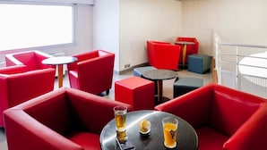 A modern interior with red seating and small round tables, some with drinks. - Appart'hotel Le Pelerin (Lourdes)