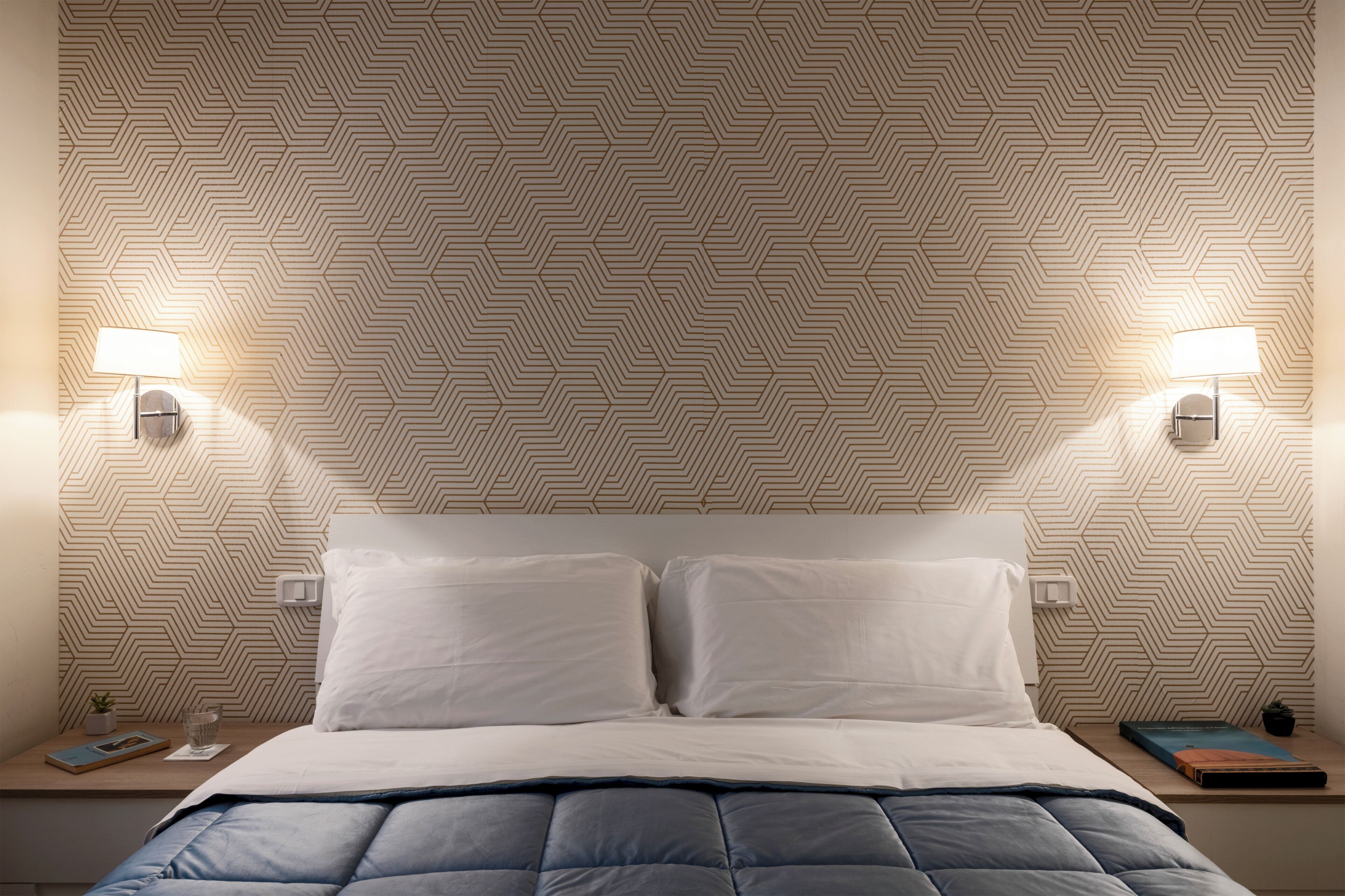 A neatly made bed with white and blue bedding, two bedside lamps, and a patterned wall.