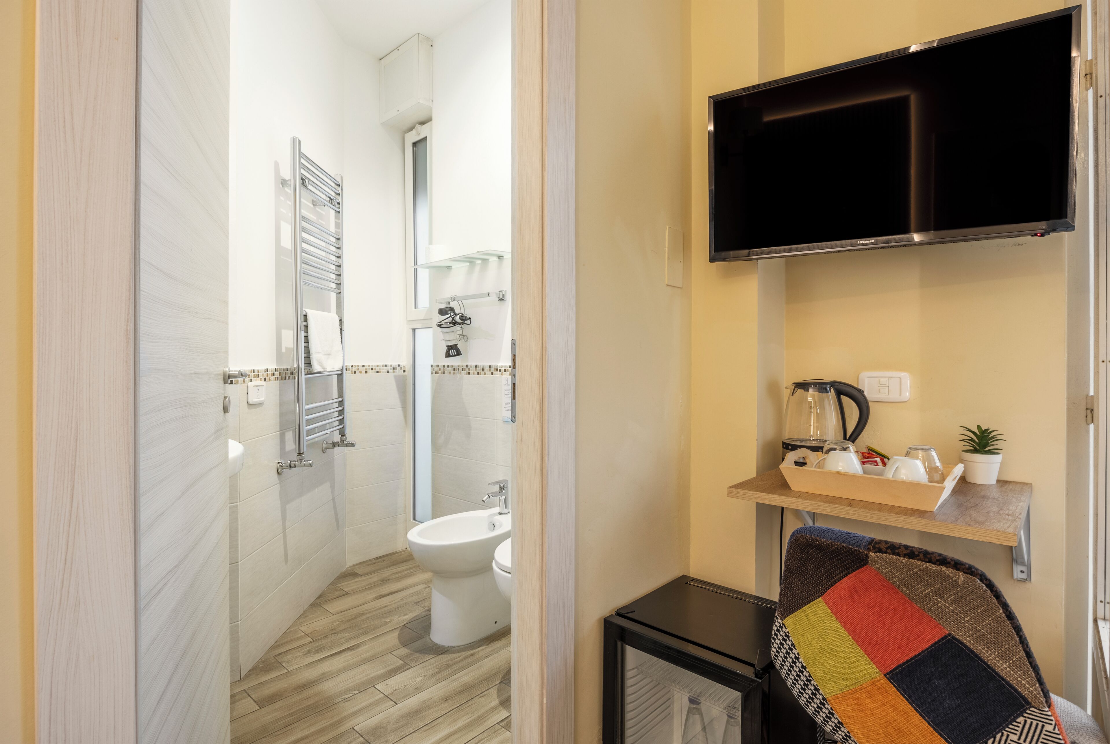 Ein kleines Badezimmer mit Toilette, Bidet und Handtuchhalter. Eine kleine Ablagefläche beherbergt Pflegeprodukte und eine Pflanze.